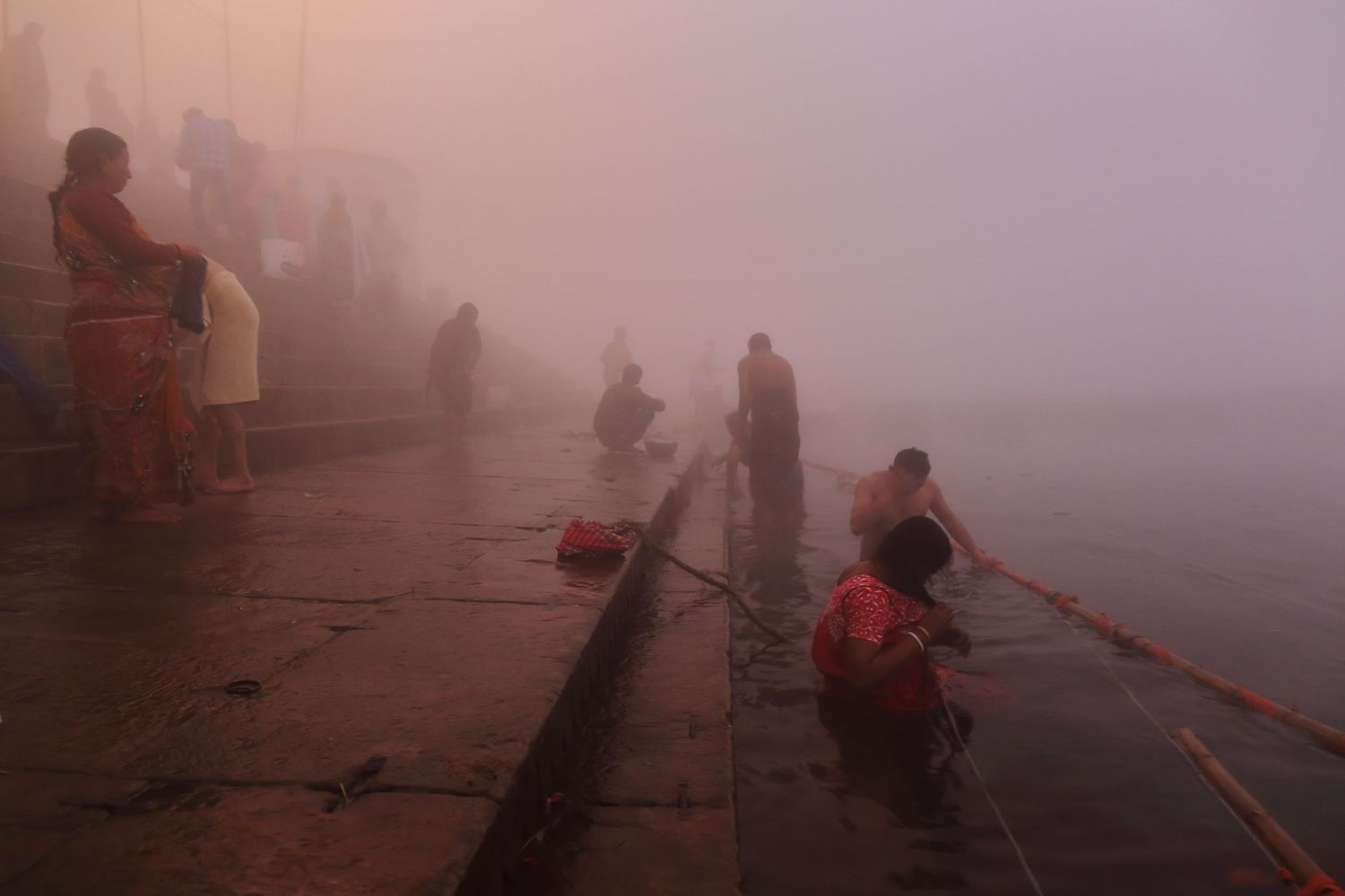 Foggy scene at Varanasi ghats with silhouettes of devotees performing morning rituals.