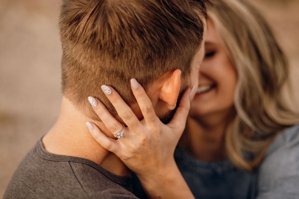 Intimate close-up of a couple embracing with focus on her hand displaying an engagement ring.