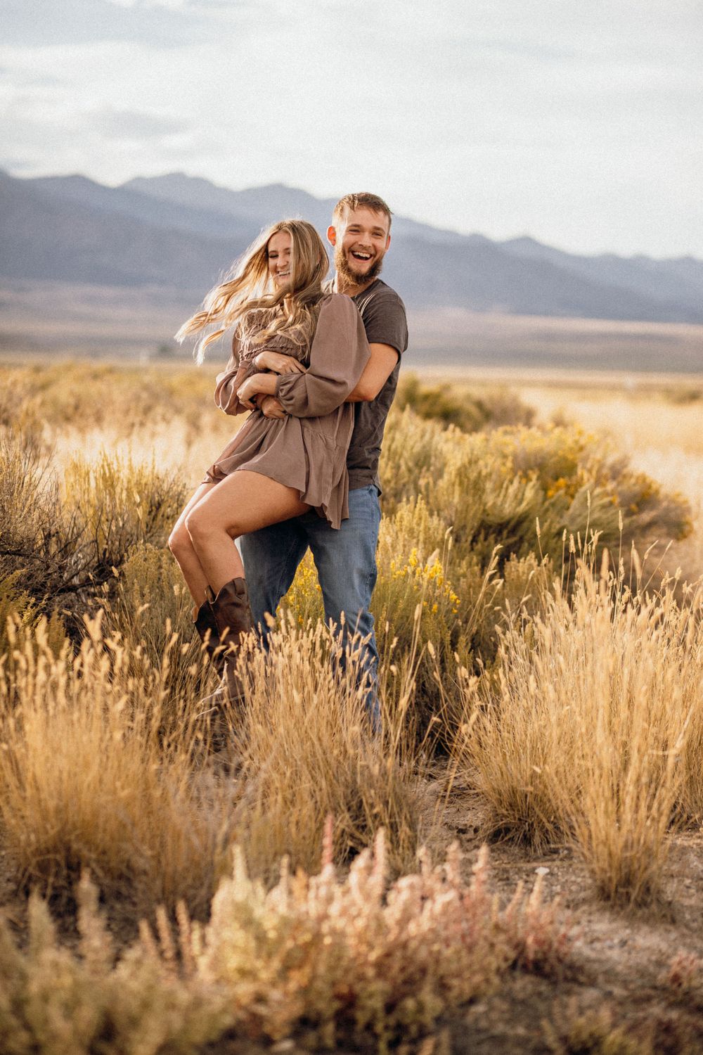 Romantic couple embracing in desert landscape with mountains in background.