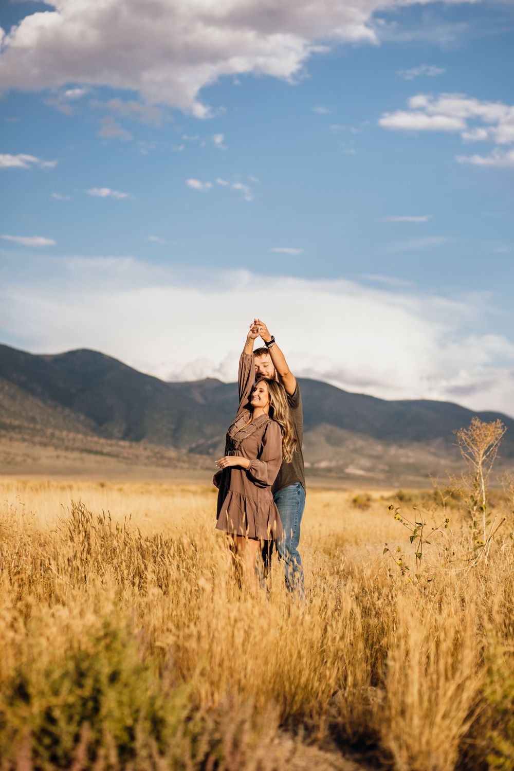 Couple dancing together in field of tall grass with mountains behind them.