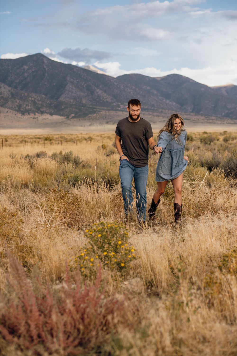 Two people standing in a field of tall grass with mountains behind them at sunset.