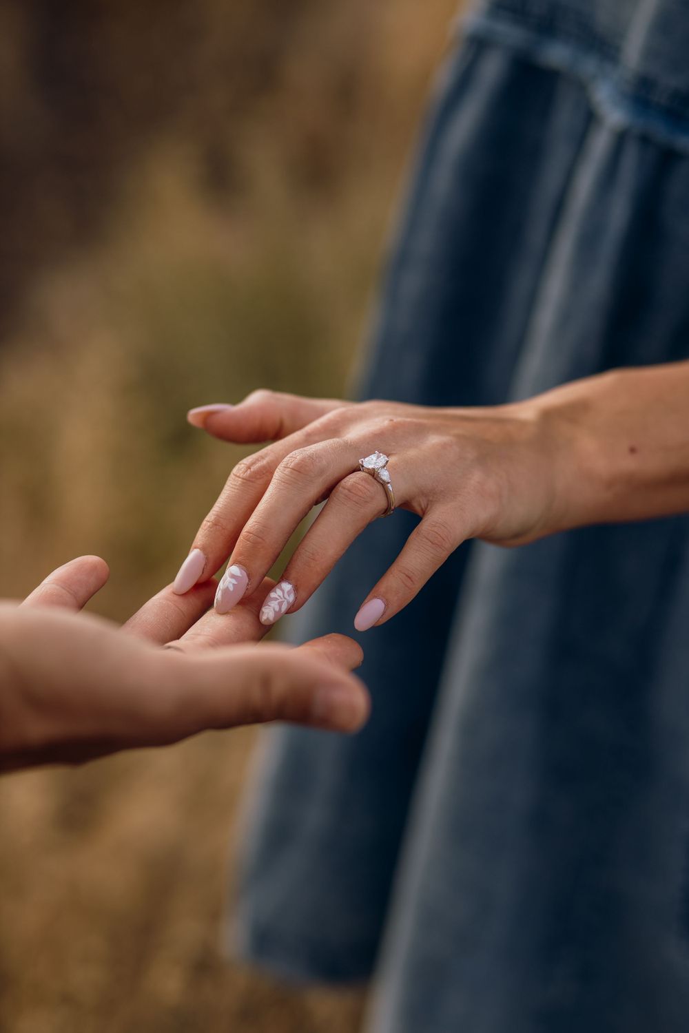Close-up of hands with an engagement ring during a tender moment outdoors.