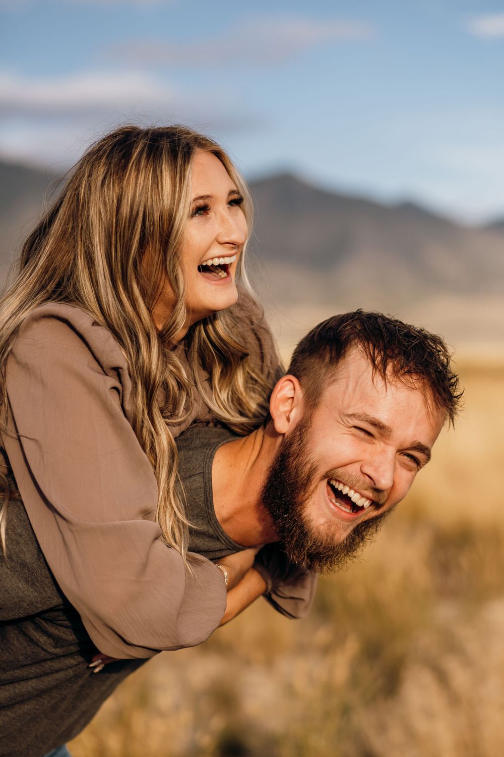 Happy couple sharing playful piggyback ride moment against desert mountain backdrop.