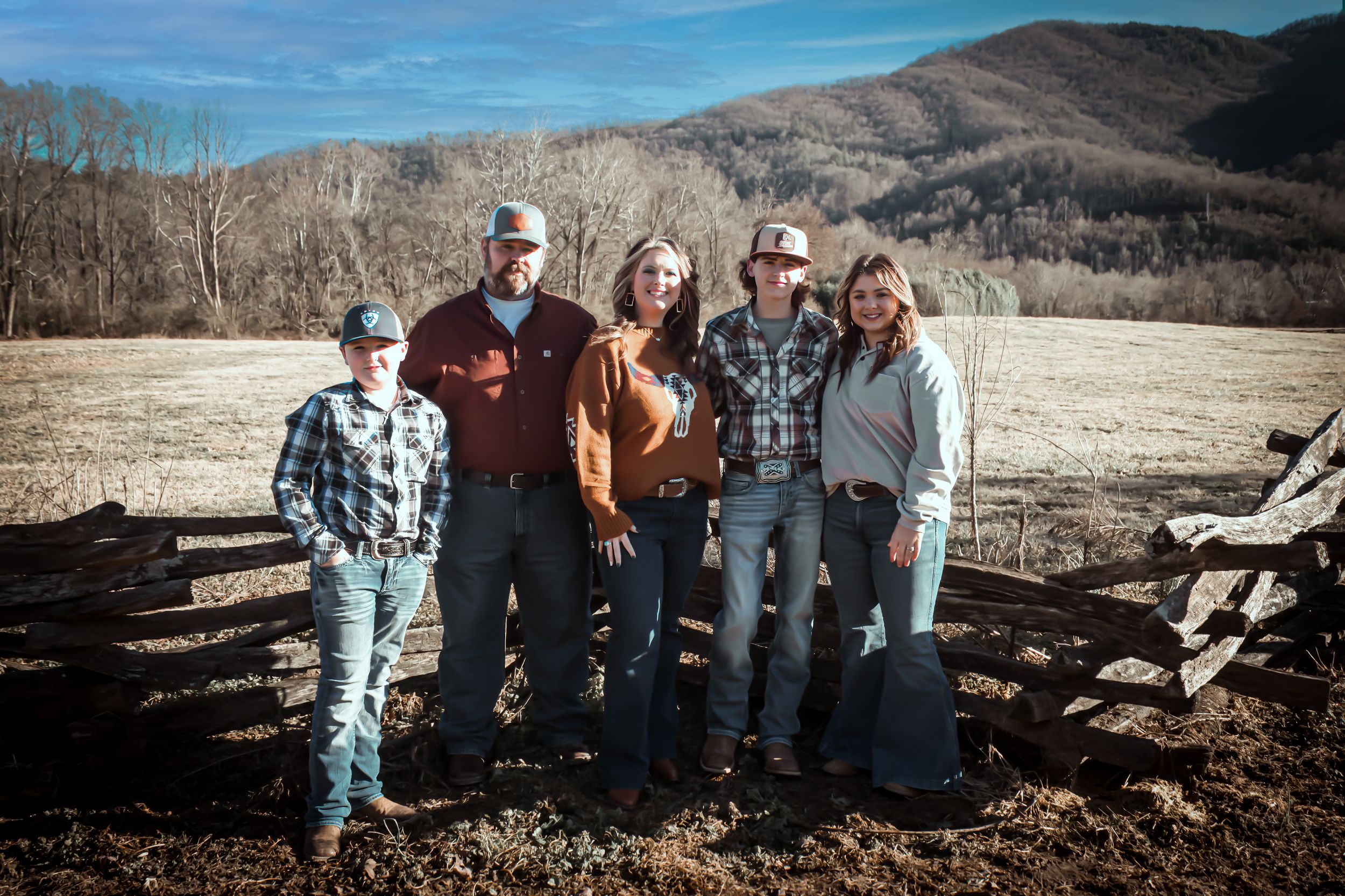 A group of people pose together in front of a mountainous rural landscape on a sunny day.