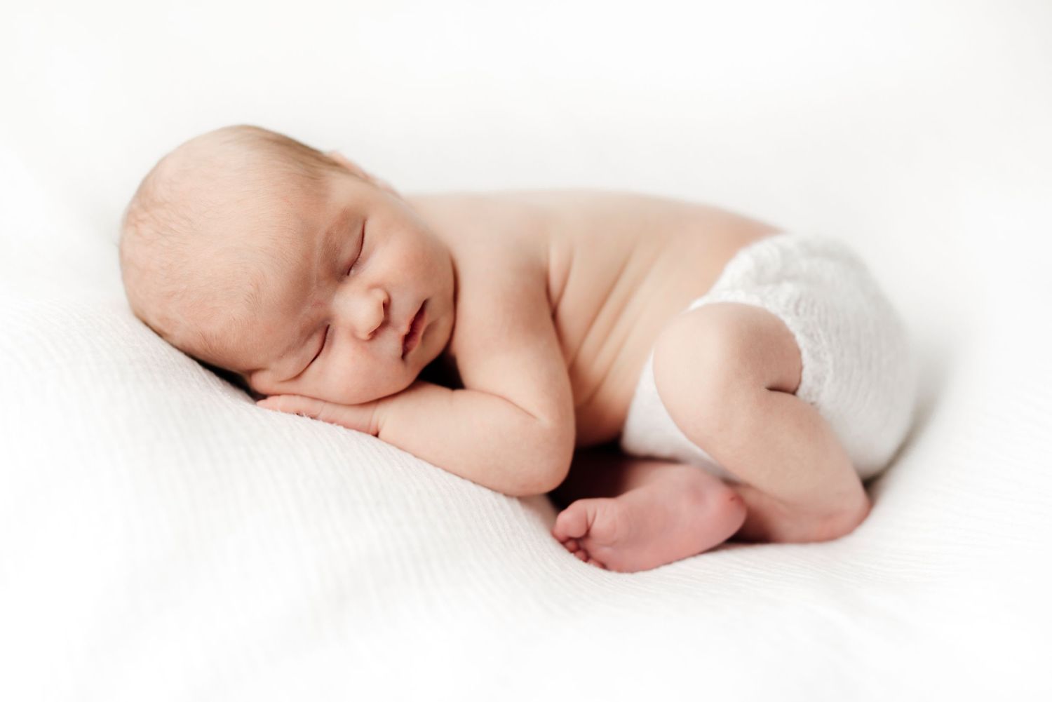 Peaceful sleeping newborn baby in white diaper lying on light background.