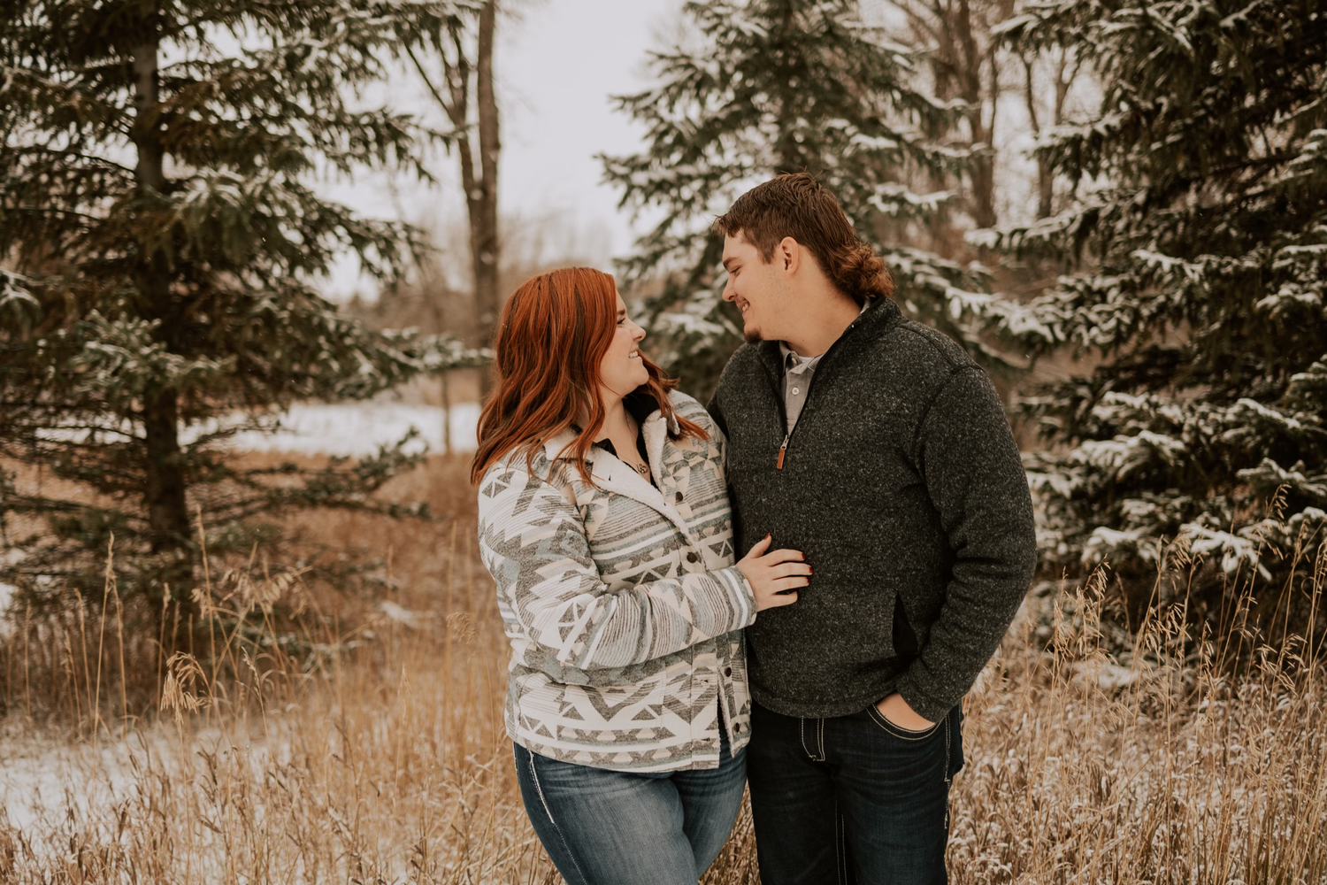 Couple sharing intimate moment among evergreen trees in sepia toned photography.