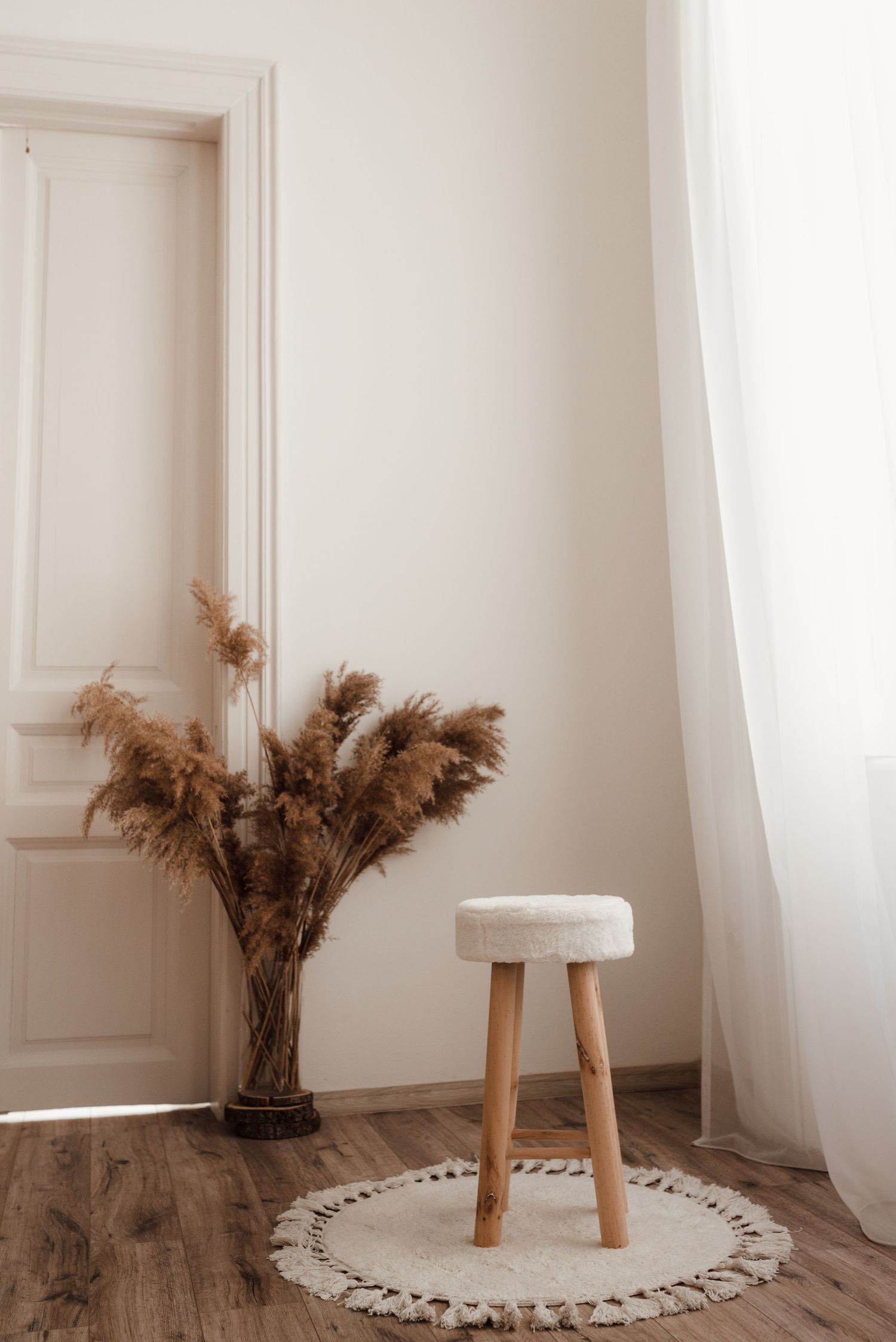 Minimalist corner decor with wooden stool, pampas grass in vase, and circular rug on wood floor.