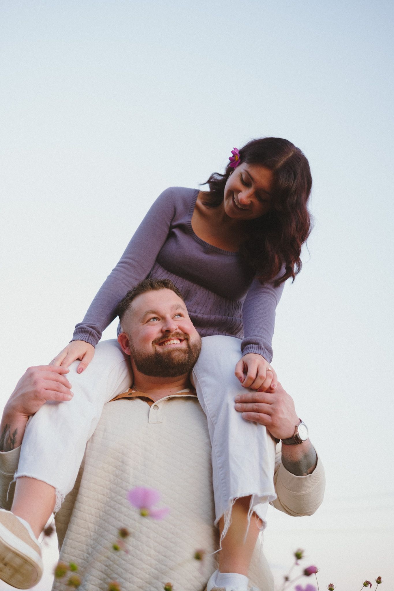 A playful couple embraces outdoors during a photo session with flower petals.