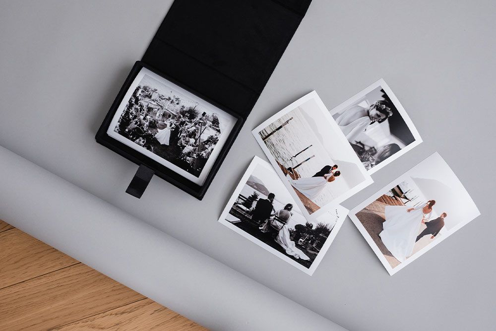 Black photo album with vintage photographs scattered on gray surface.