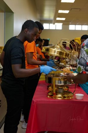 People serving themselves food from golden chafing dishes at a buffet setup with red tablecloth.