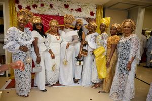 A festive celebration featuring guests wearing traditional Nigerian attire in white and gold with elegant headwraps.