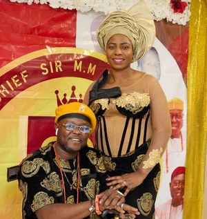 Couple in matching black and gold formal attire pose in front of decorative banner.