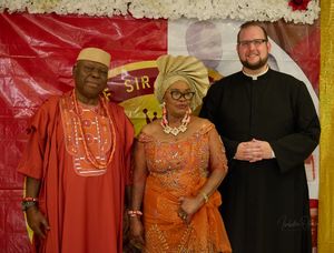 Group photo with people wearing traditional African and formal attire against a red backdrop.