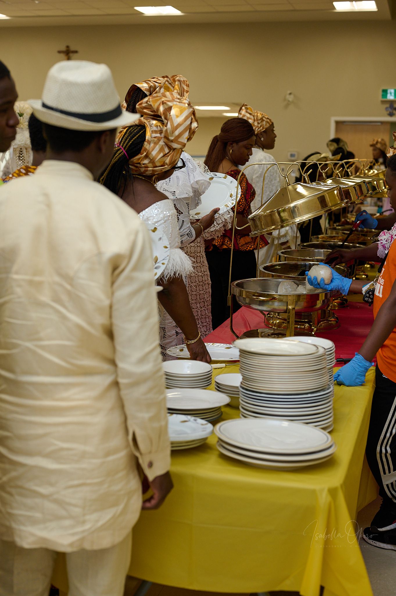 Buffet line setup with chafing dishes and stacks of white plates on a yellow tablecloth at a formal event.