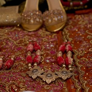 Close-up of ornate beaded jewelry and decorative shoes on red embroidered fabric.