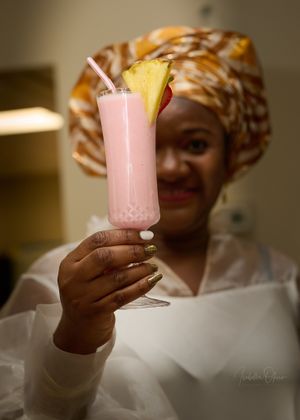 A festive pink tropical smoothie garnished with pineapple and a straw being held up for display.