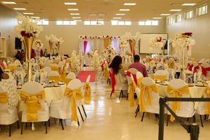 Elegant event hall decorated with floral centerpieces, white chairs, and yellow tablecloths.