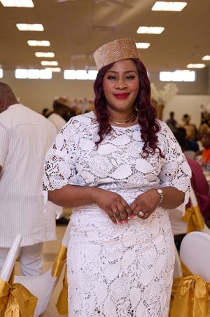 A woman in an elegant white lace dress and sparkly hat smiles at a formal event.