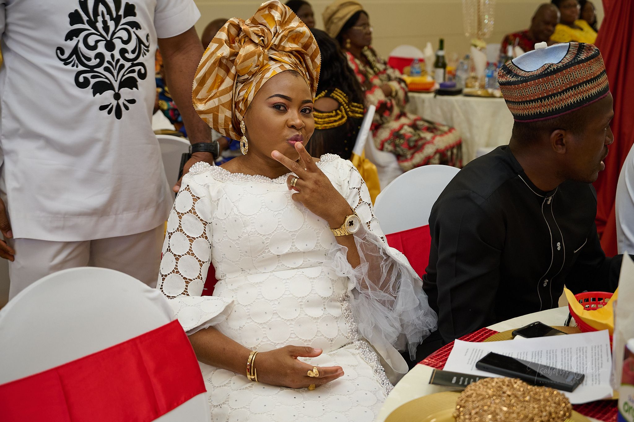 Guests in traditional white attire and headwraps enjoying a formal celebration at decorated tables.