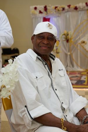 Guest in white attire and baseball cap seated at decorated event venue.