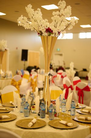 Elegant table setting with tall gold vase centerpiece featuring white flowers and red accents.