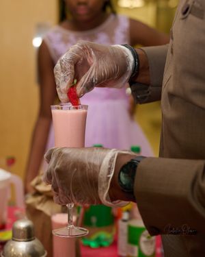 Hands in gloves preparing pink cocktails at a bar or event.