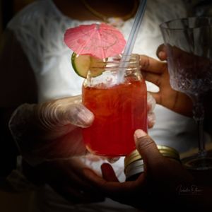 Red cocktail garnished with citrus and pink umbrella being served in mason jar.