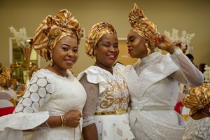 Three guests in elegant white and gold traditional attire with matching headwraps posing together.
