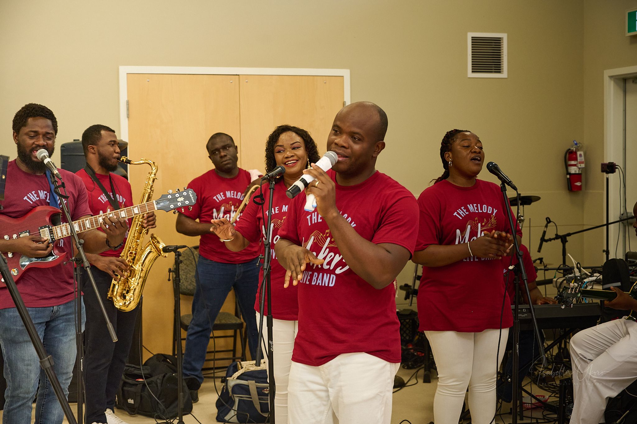 Live band in red uniforms performs with saxophone and singers at indoor event.