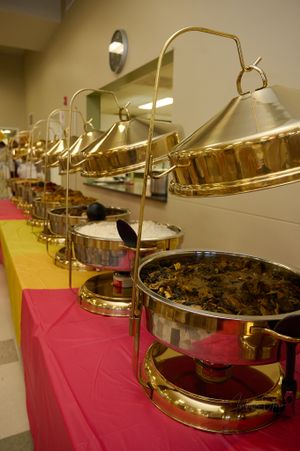 Row of golden chafing dishes set up on a buffet table with red tablecloth.