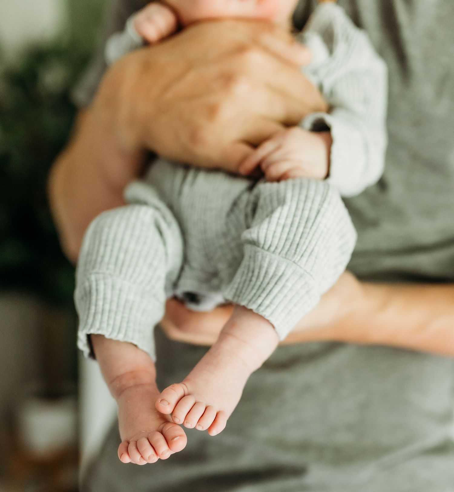 Close up of tiny baby feet in gray knit clothing held by caring hands.
