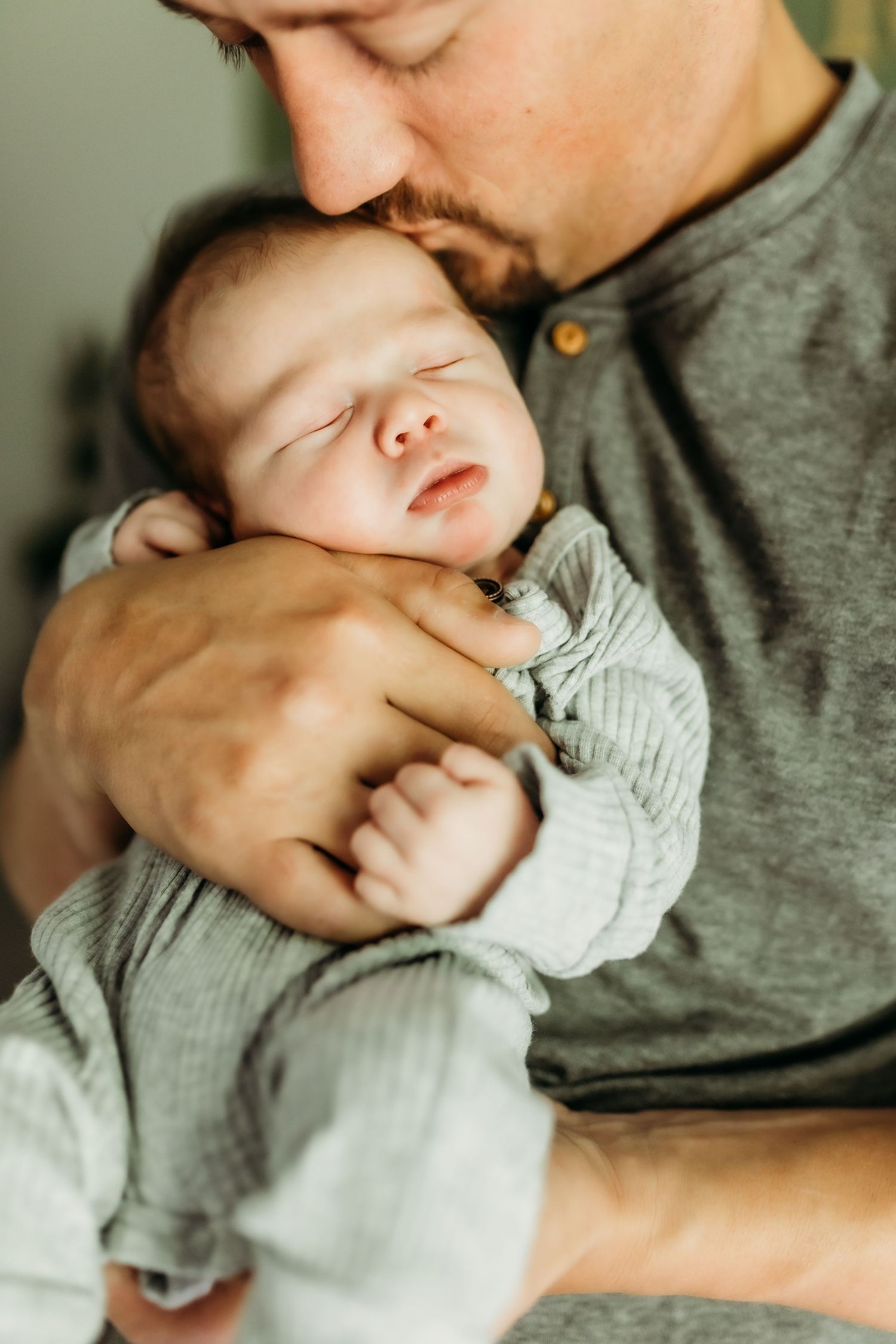 A sleeping newborn baby in a gray outfit being cradled against someone wearing a gray shirt.