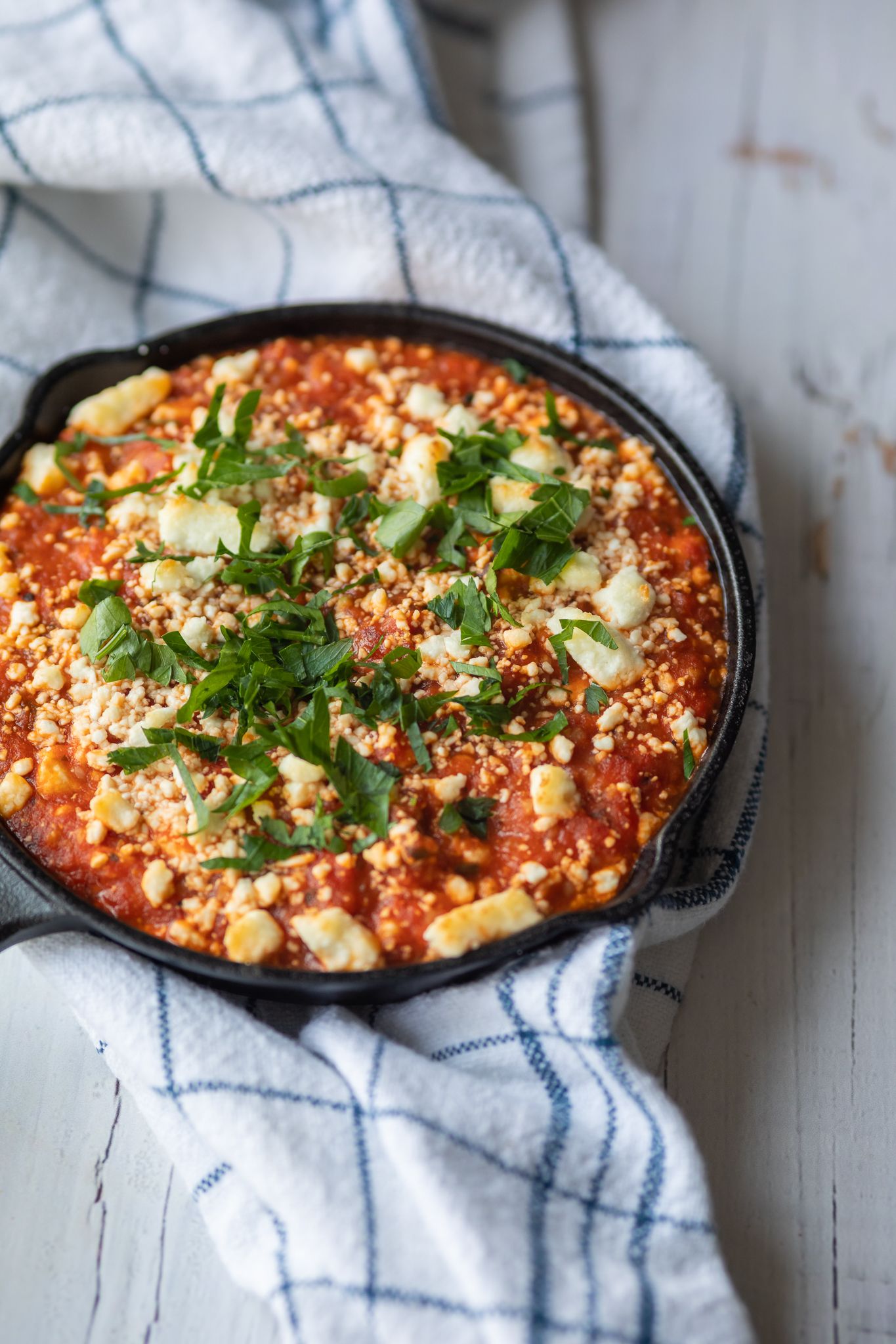 Baked pasta dish with red sauce and melted cheese garnished with fresh herbs.
