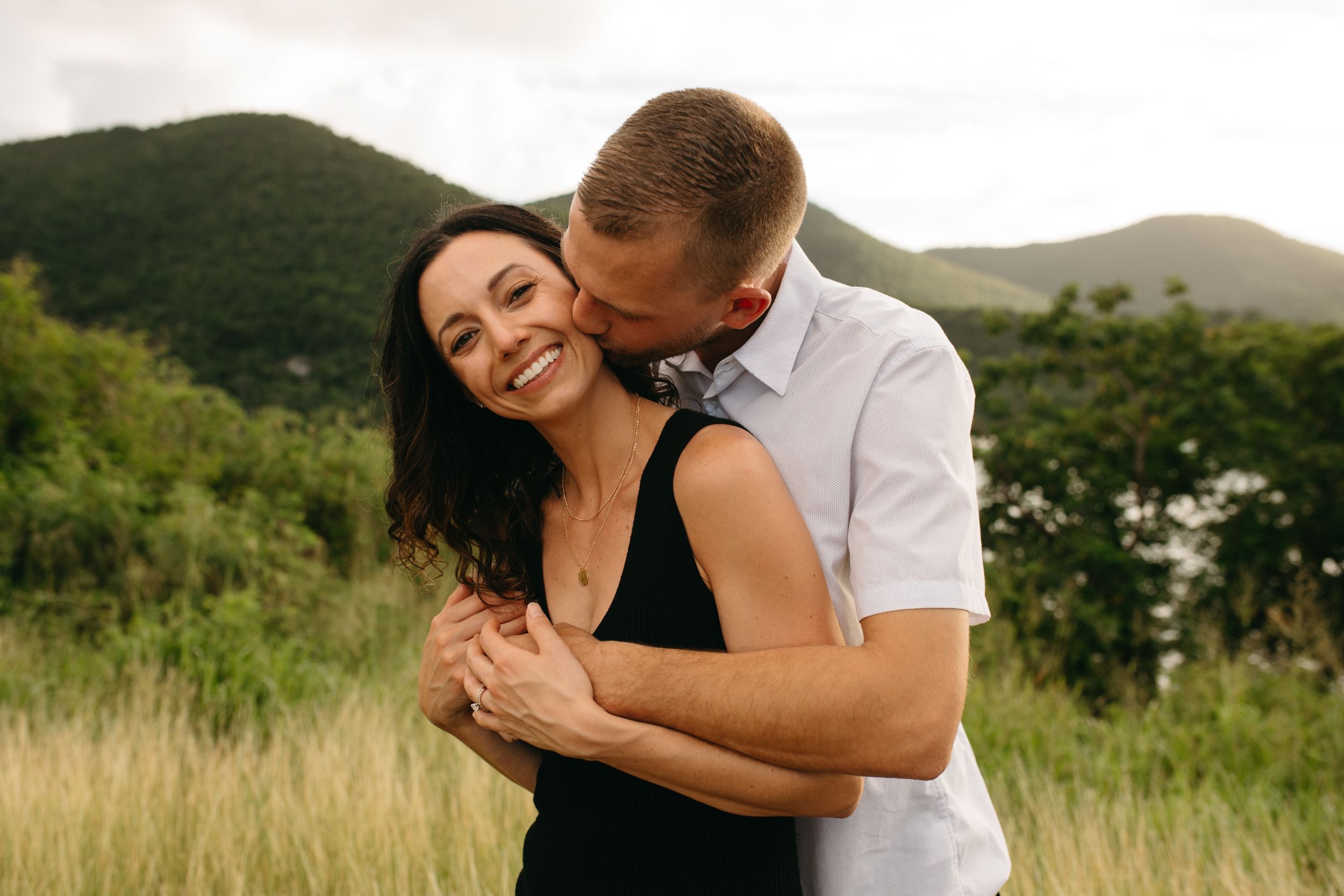 A joyful couple embracing in a scenic mountain meadow during golden hour.