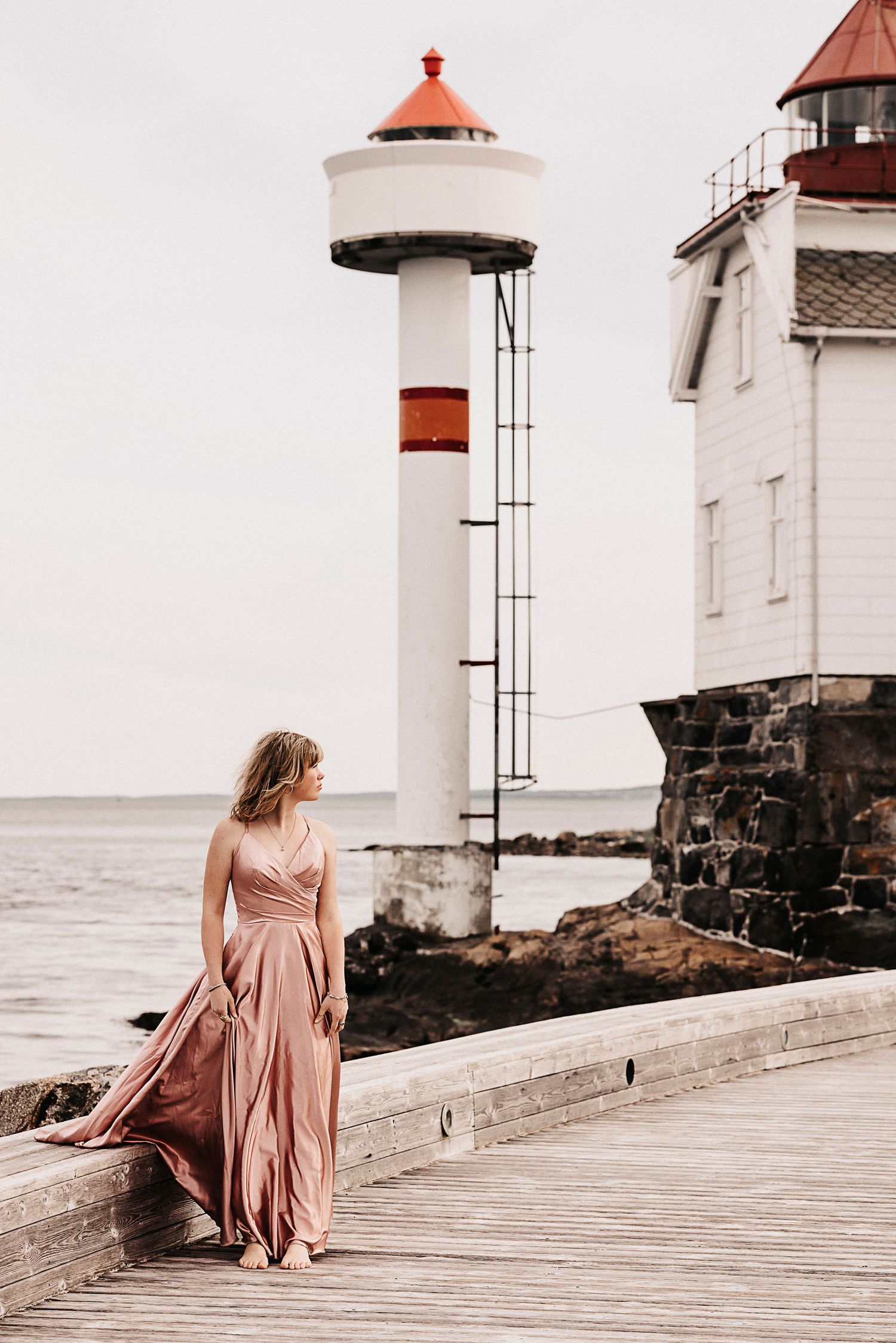 A romantic seaside portrait with a flowing mauve dress against a white lighthouse backdrop.