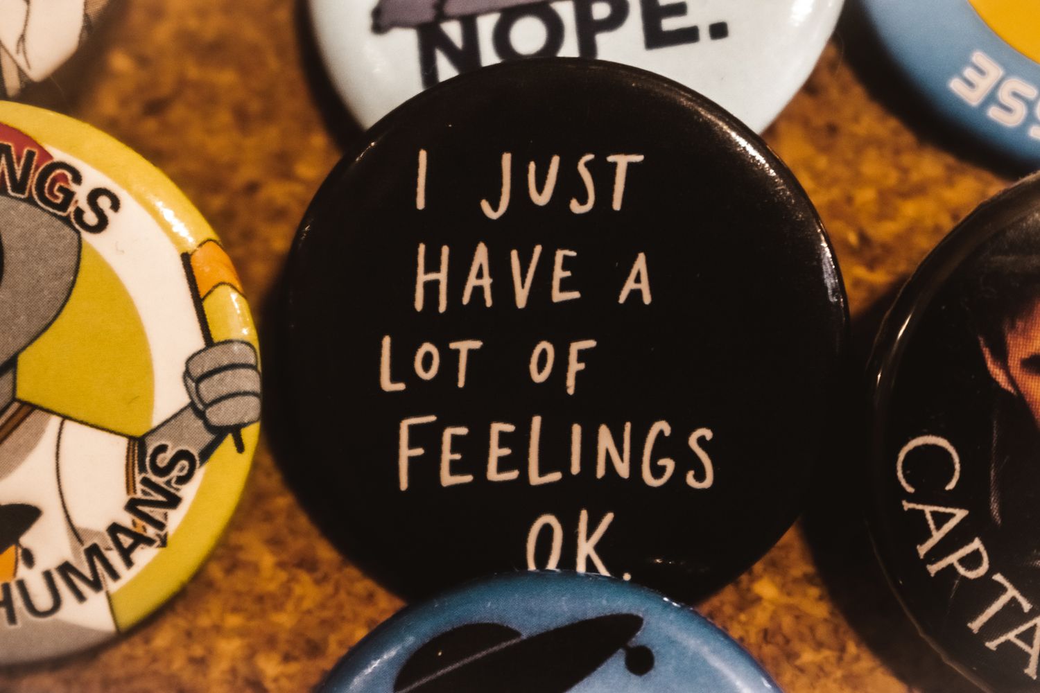 A black button pin with white text that reads "I JUST HAVE A LOT OF FEELINGS OK" among other pins.