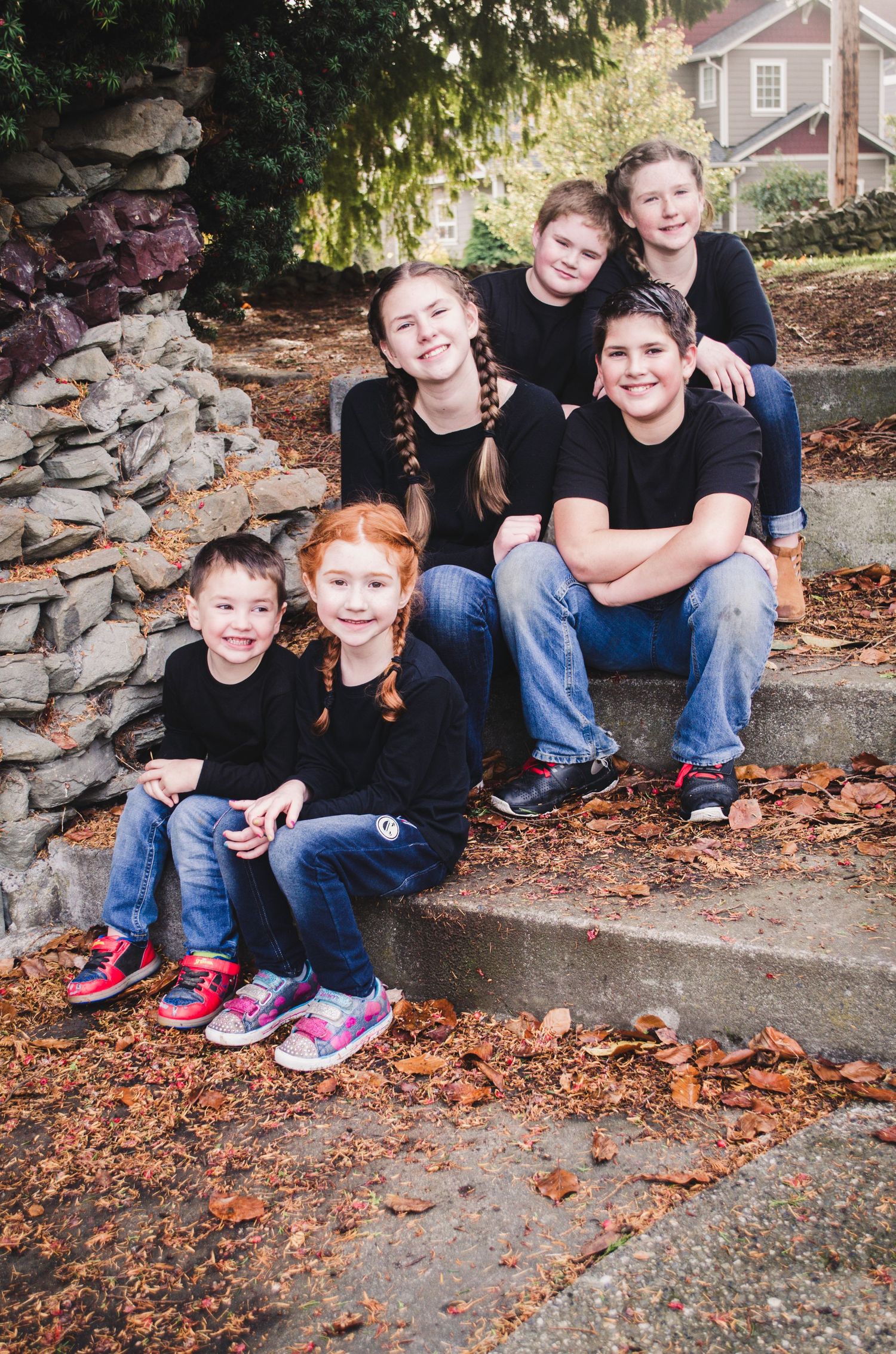 A group wearing matching black shirts sits on stone steps covered in autumn leaves.