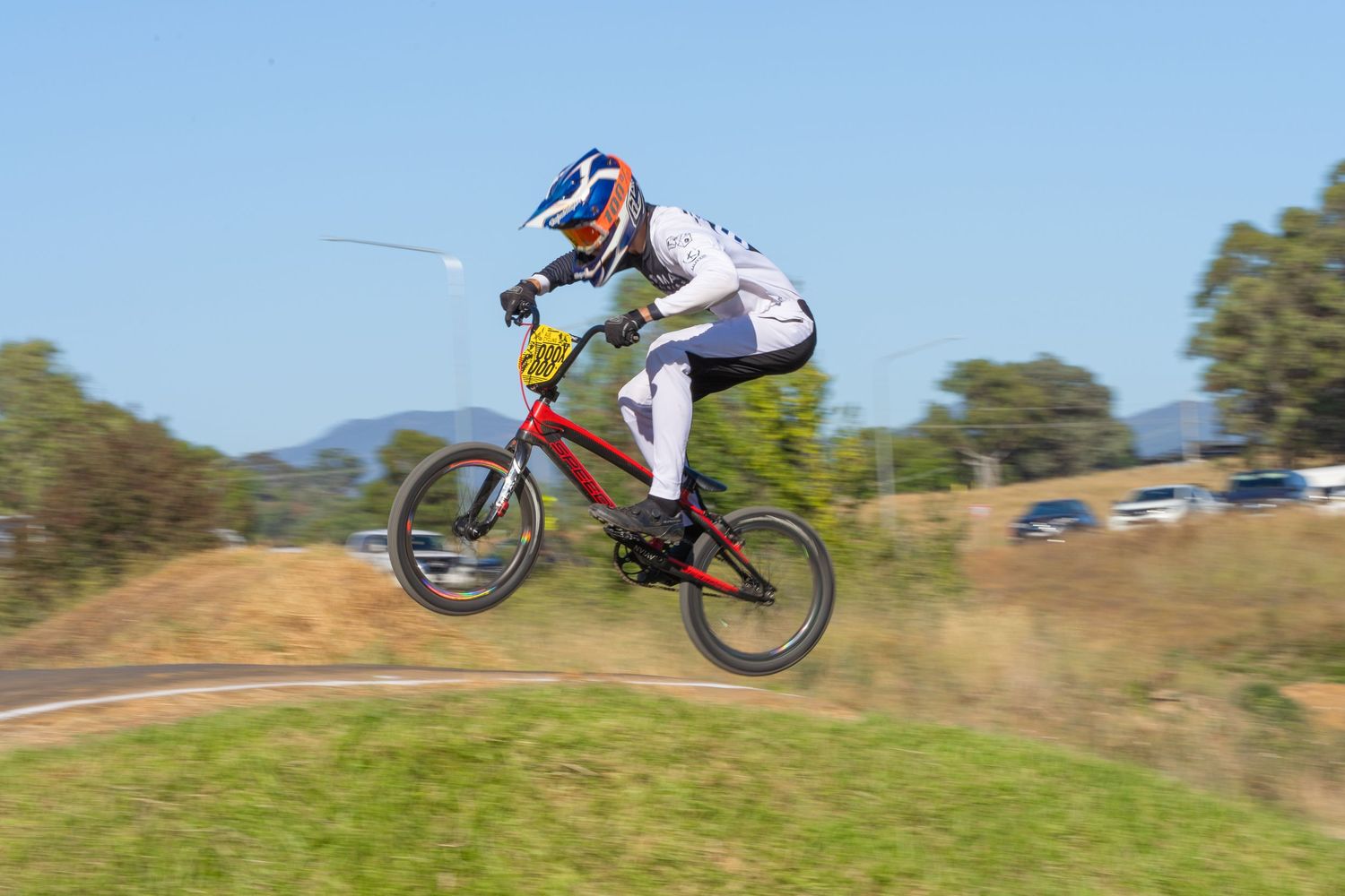 BMX rider performs aerial jump on dirt track against blue sky.