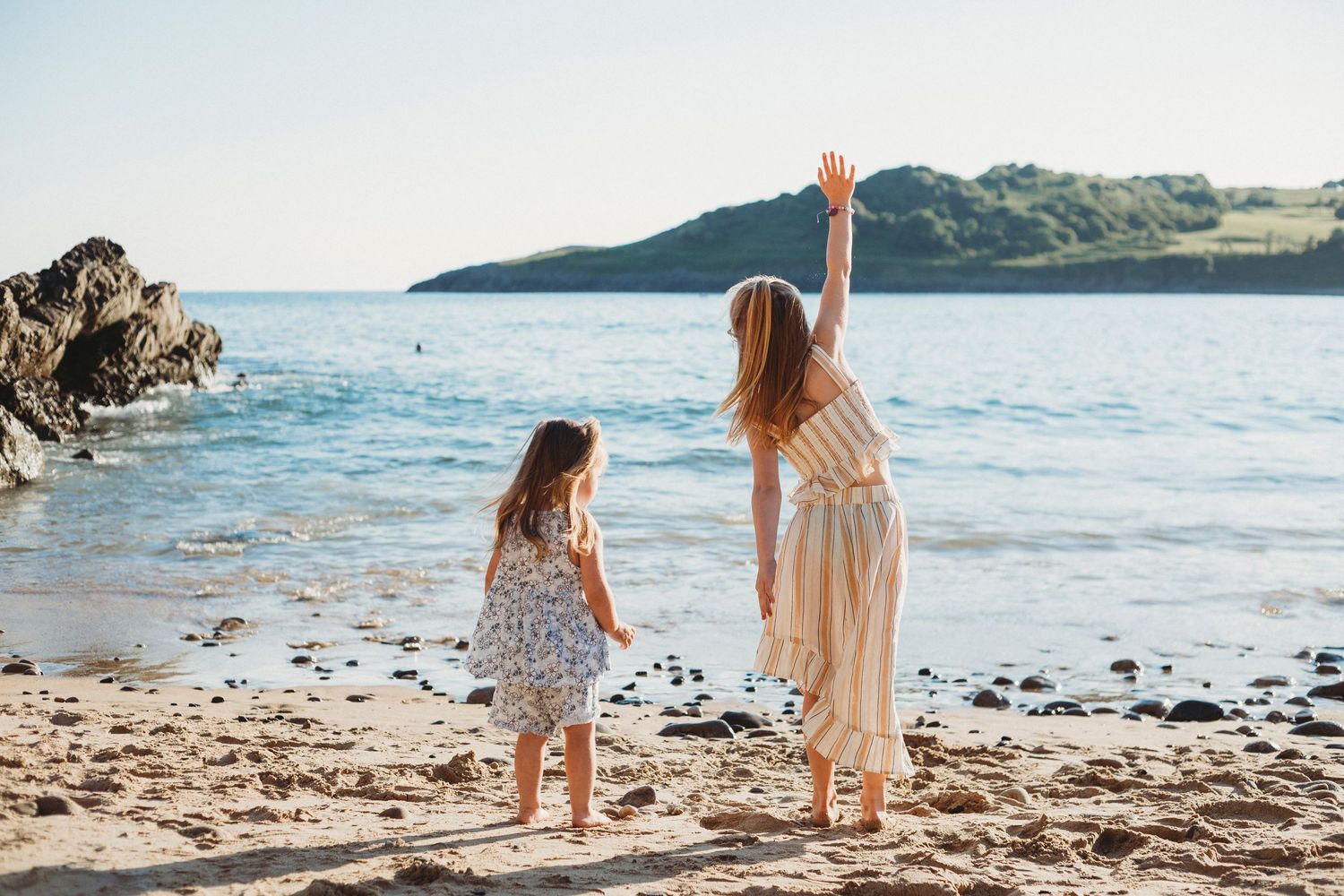 People enjoying a sunny day on a beautiful coastal beach with hills in background.