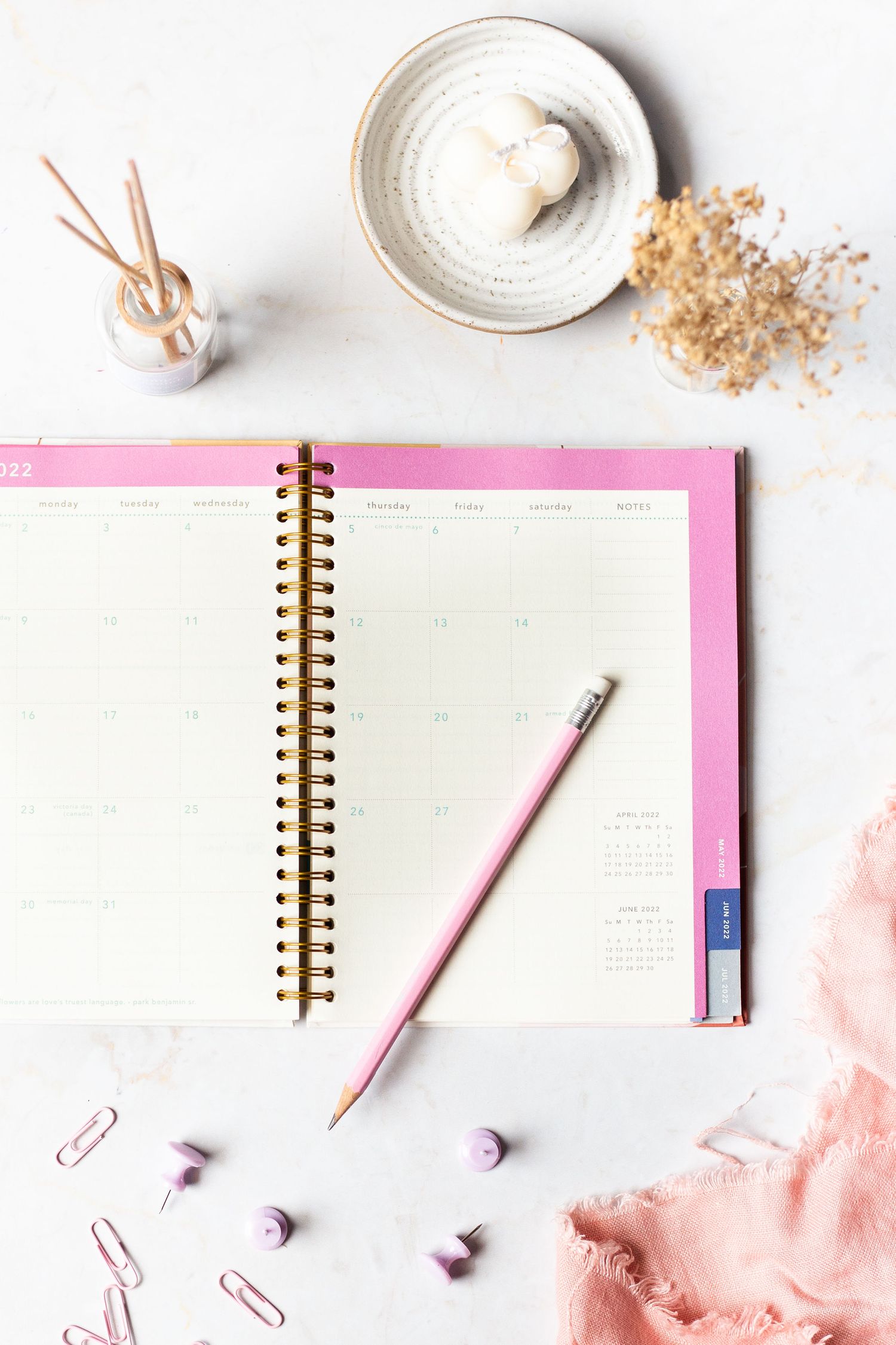 Pink planner notebook with pencil and decorative accessories on white background.