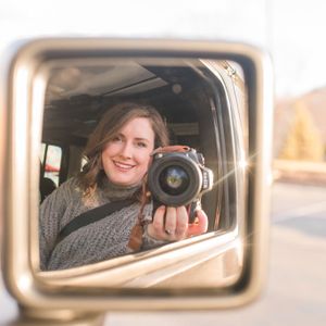 A reflection in a side mirror shows someone taking a photo with a camera.