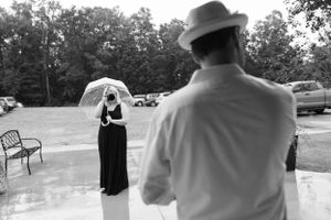 Two people with umbrellas standing in the rain at an outdoor event.