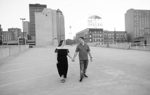 Two people holding hands walk together on a rooftop parking area with city buildings in the background.