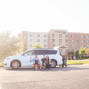 A white minivan parked outside a Courtyard hotel with people and luggage nearby.
