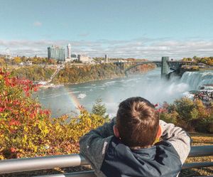 Person looking out over Niagara Falls with autumn foliage and city buildings in the background.