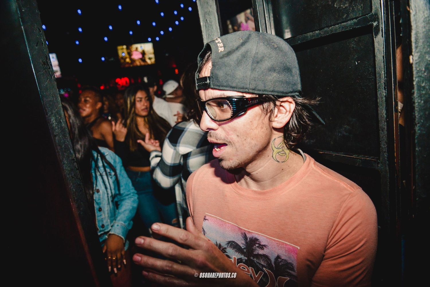 Person in orange shirt and cap gesturing at a dimly lit nightclub venue.