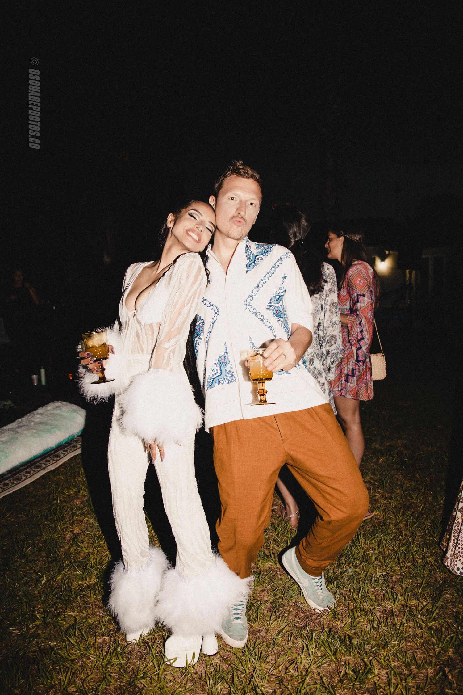 Couple in coordinating white and blue outfits pose together at an outdoor evening event.