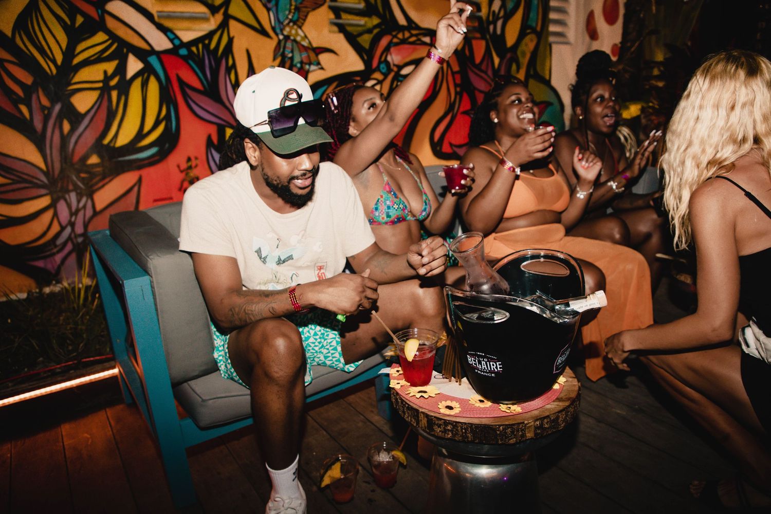 Party scene with colorful floral backdrop and people sharing food.