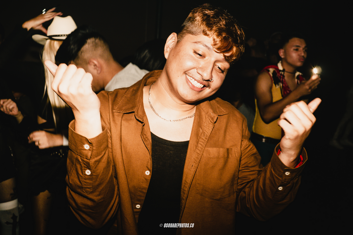 Person in brown jacket dancing enthusiastically at a dark nightclub.