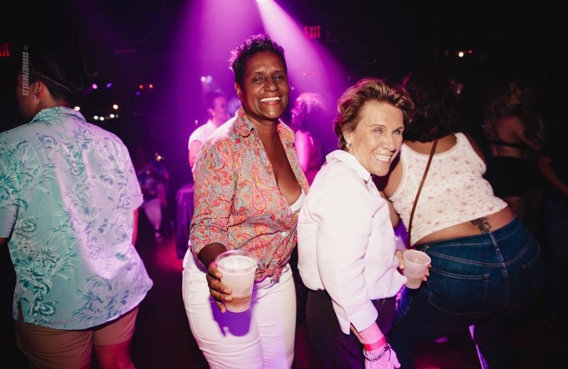 Partygoers enjoying themselves on a dance floor under purple stage lighting.